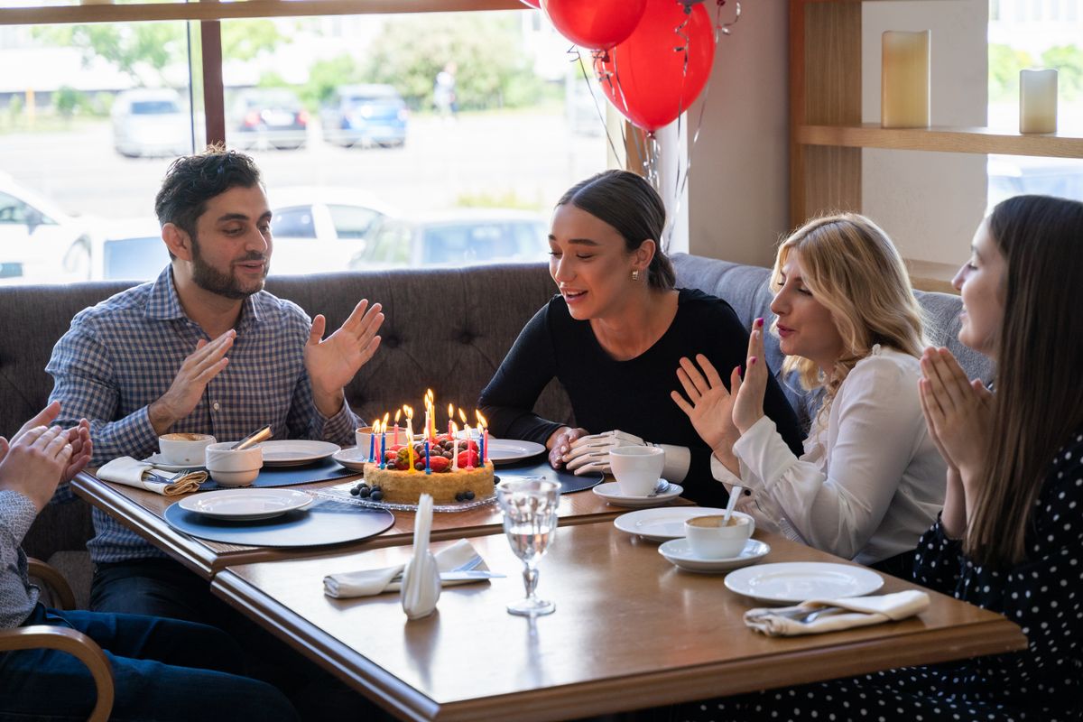 People gathered around a birthday cake at a cafe table